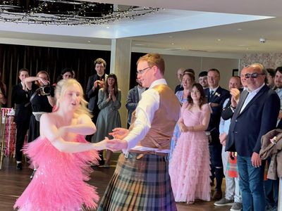 A guest in a pink gown spins with a kilted dancer as the room cheers