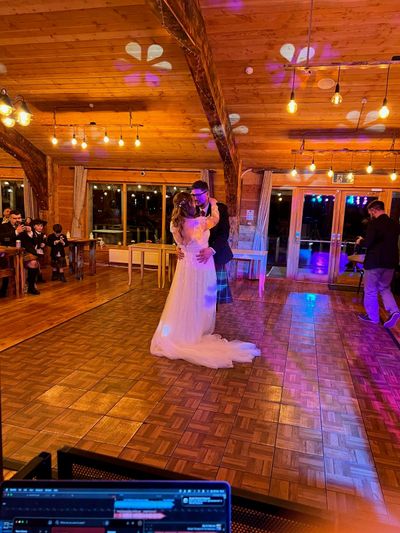 A bride takes the floor under festoon lights in a rustic wedding barn
