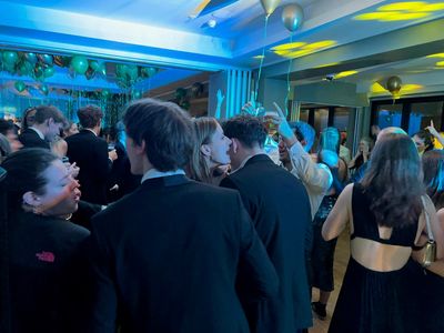 A young crowd celebrates on the dancefloor amid balloons and greenery
